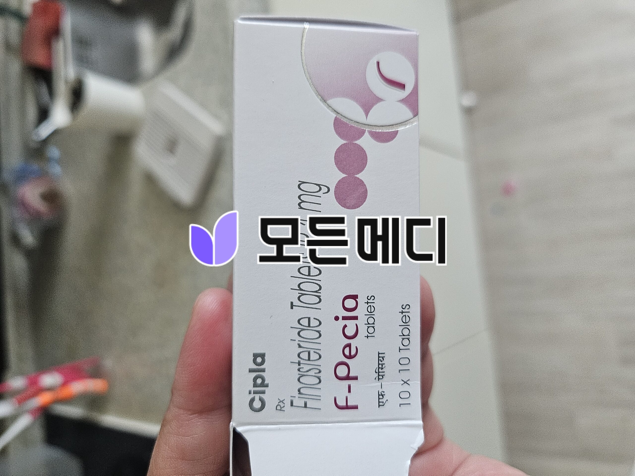 Small white supplement box with pink circular decor held in a hand; purple logo on left, clinical packaging design visible.