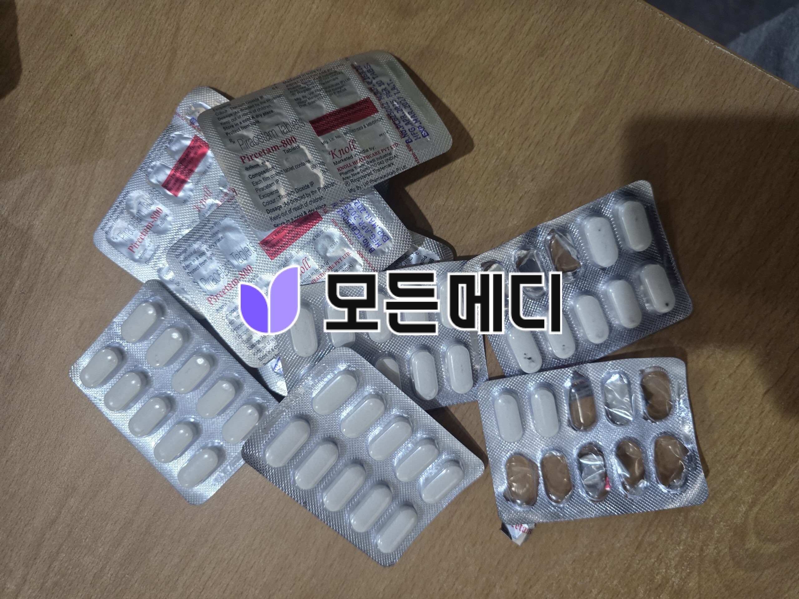 20260421_164145 | 모든메디 Blister packs containing white oval tablets scattered on a brown surface.