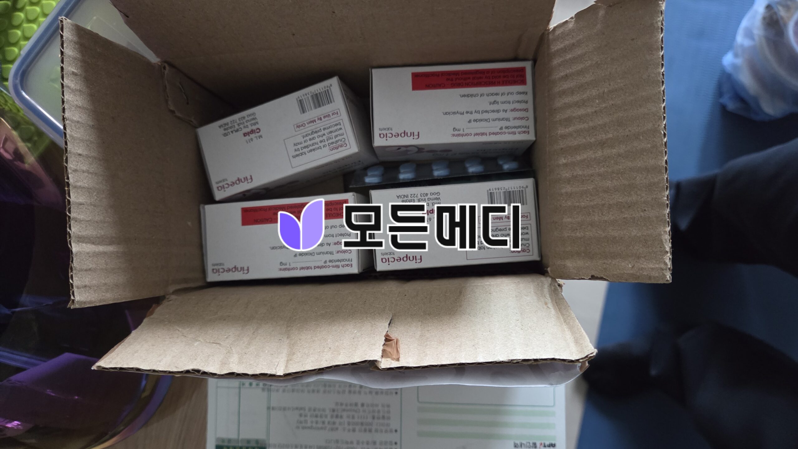 Open cardboard box containing multiple Finpecia medicine boxes arranged inside, with red warning labels visible on the packaging.