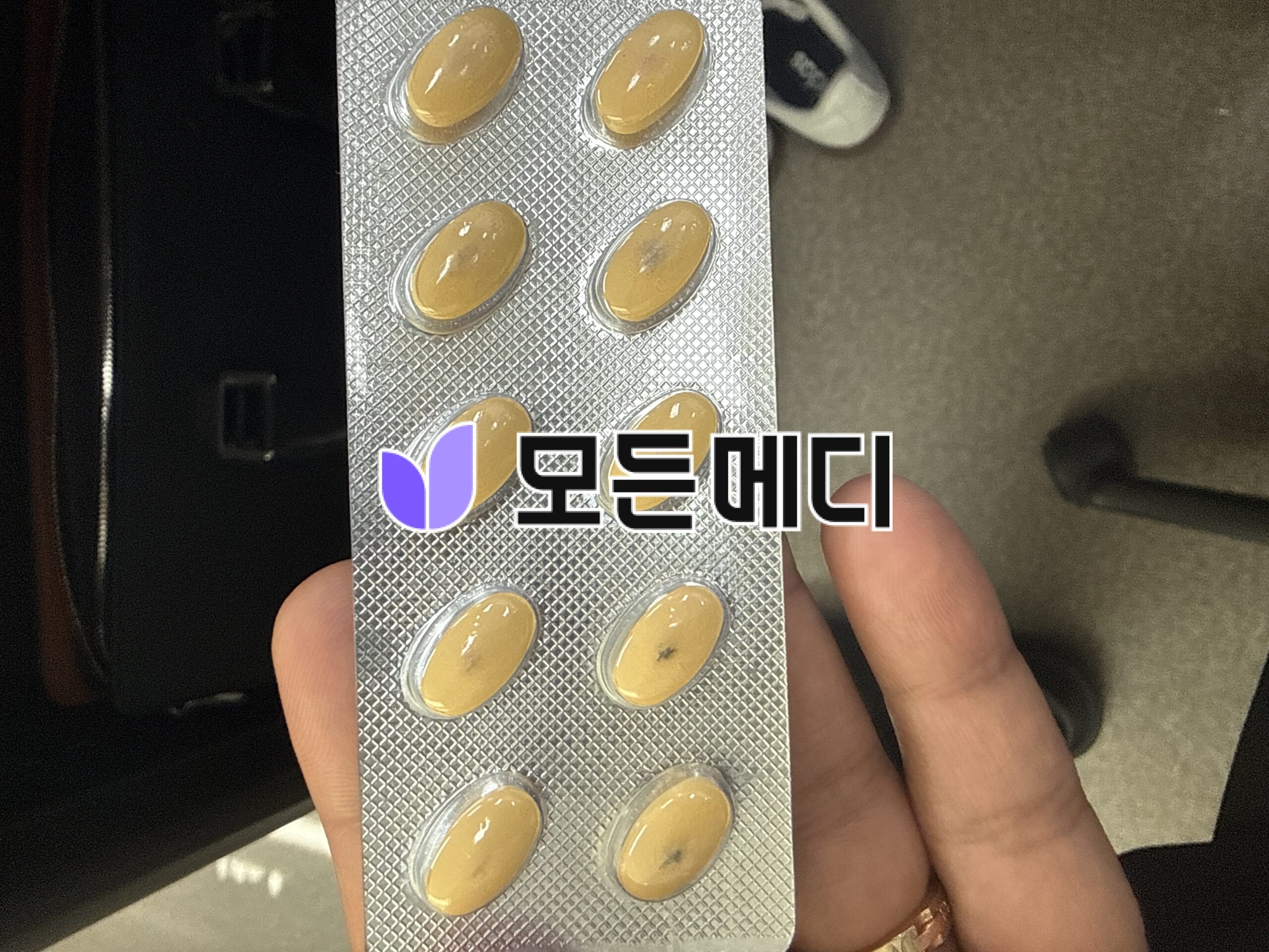 Blister pack with yellow oval capsules held between fingers.