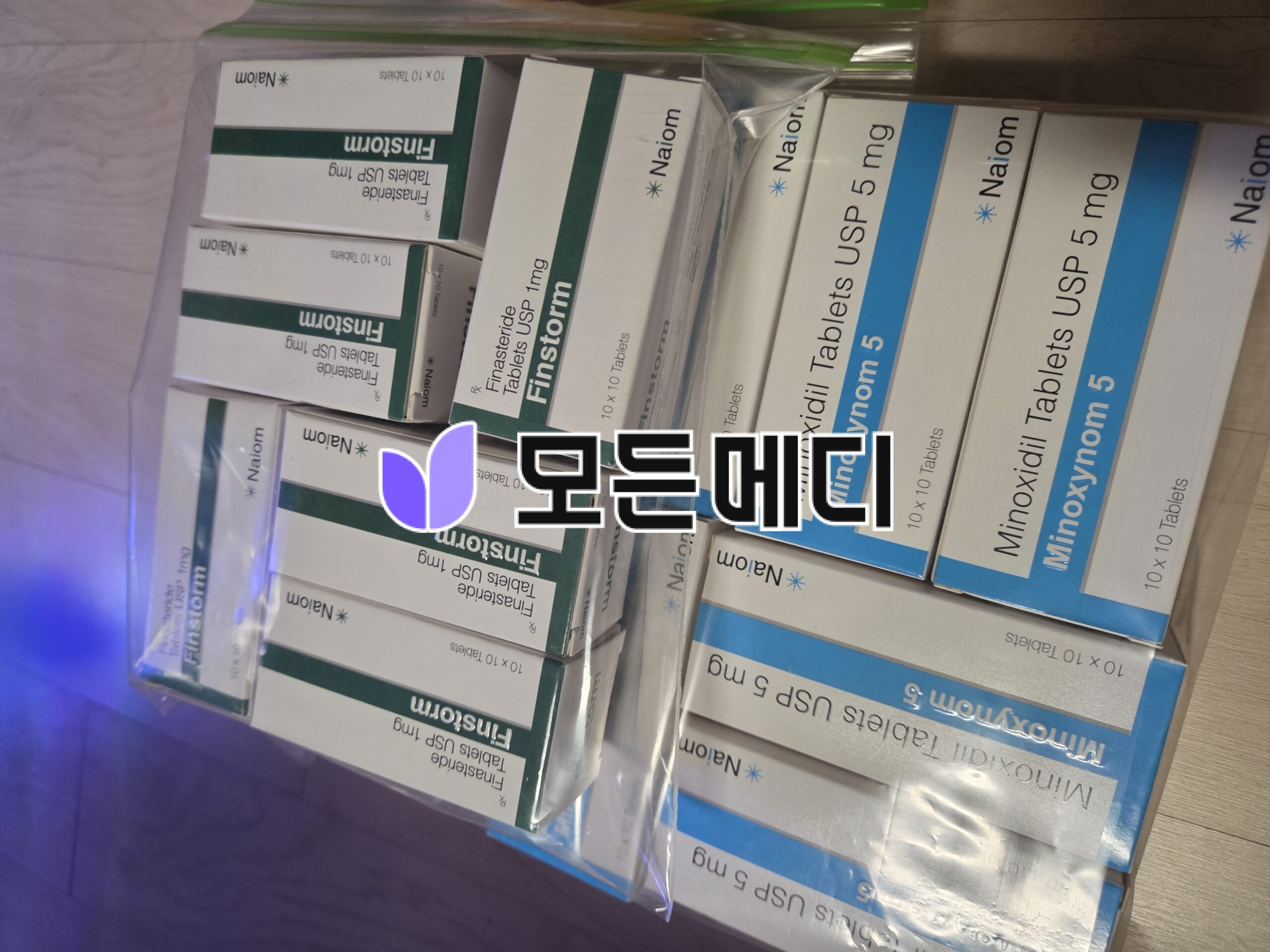 Stack of medicine boxes with green and blue bands, labeled Finasteride and Minoxidil, arranged in a container.