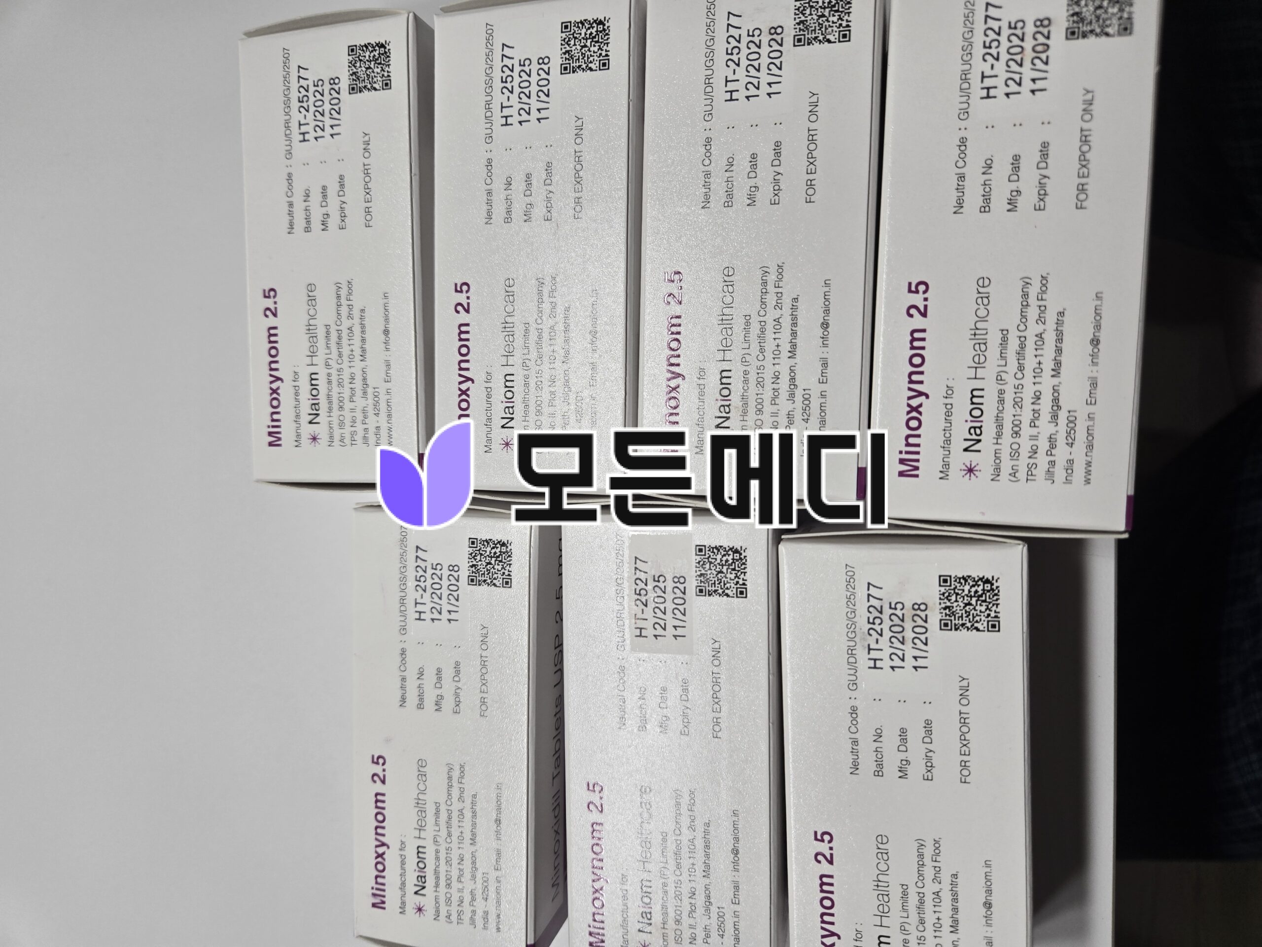 Row of white pharmaceutical boxes with purple branding, QR codes and expiry dates visible in a stacked arrangement