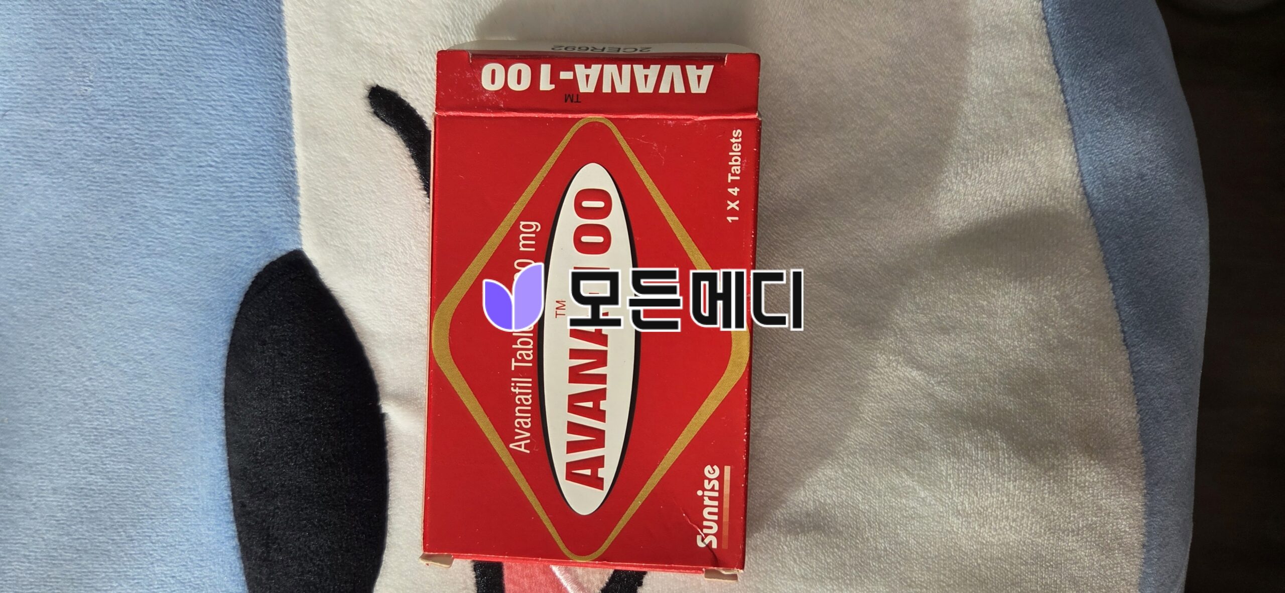 Red box labeled Avana-100 tablets on a blue/gray blanket.