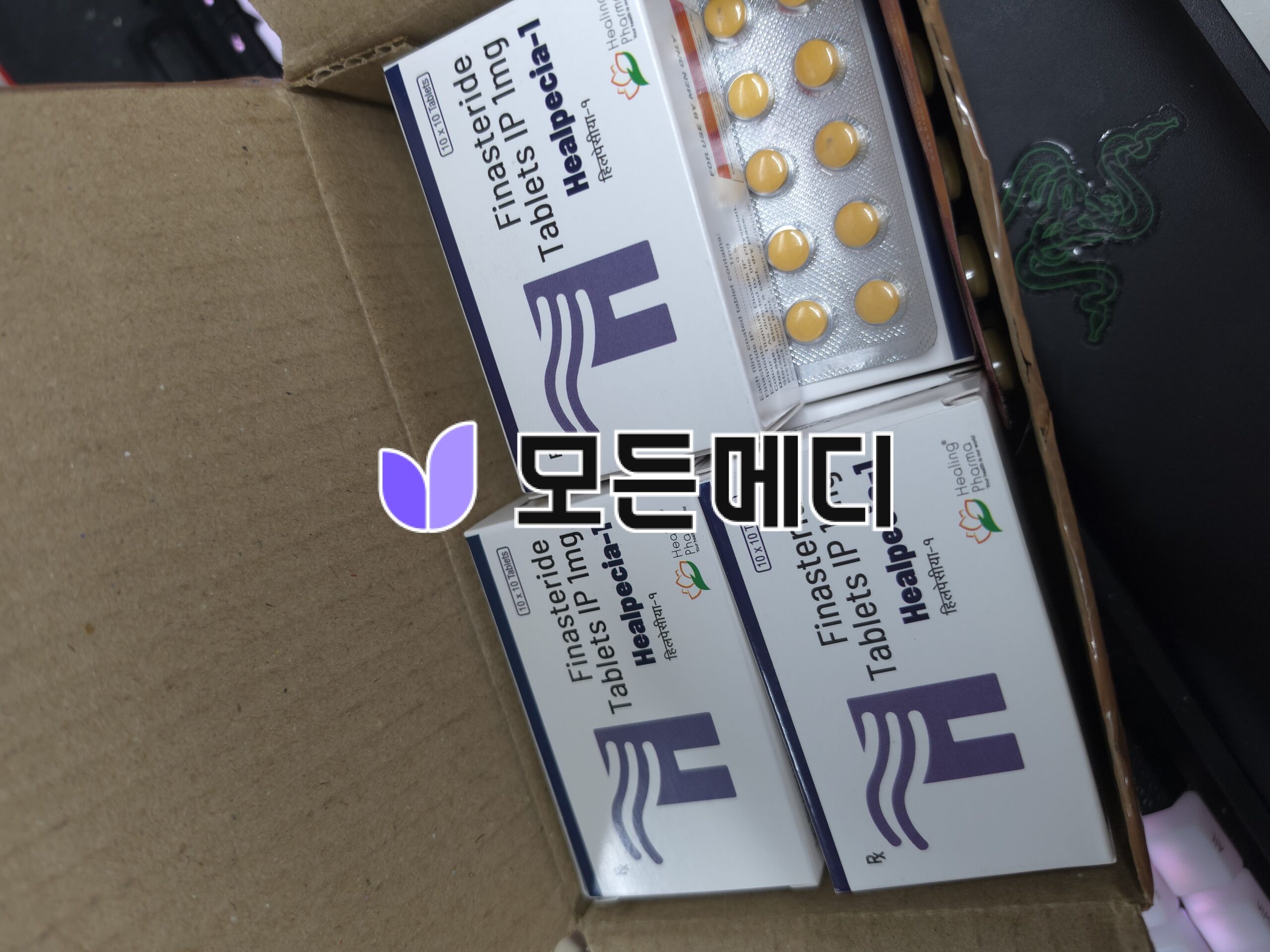 Box of finasteride tablets IP with yellow round pills in blister packs inside a cardboard box.