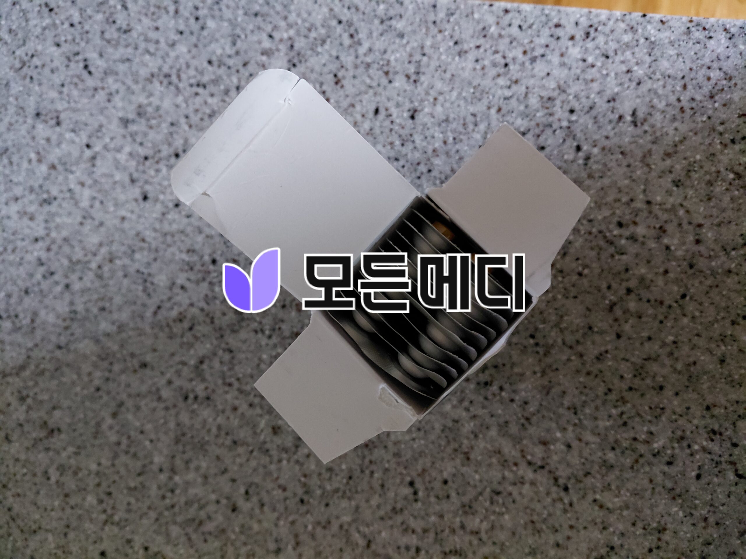 Close-up of a white box with a purple logo and bold black lettering, partially opened to reveal a ribbed black insert, on a speckled countertop.