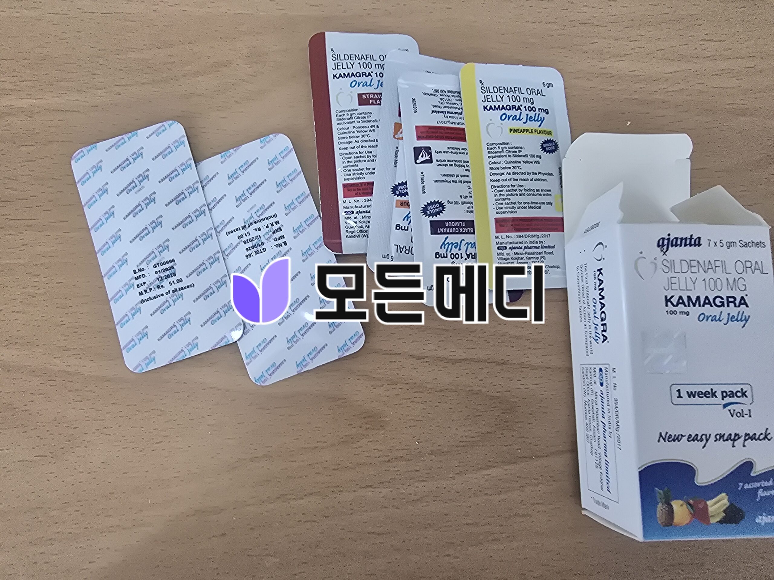 Assorted Sildenafil/ Kamagra oral jelly sachets on a wooden surface with a white one-week pack box nearby.