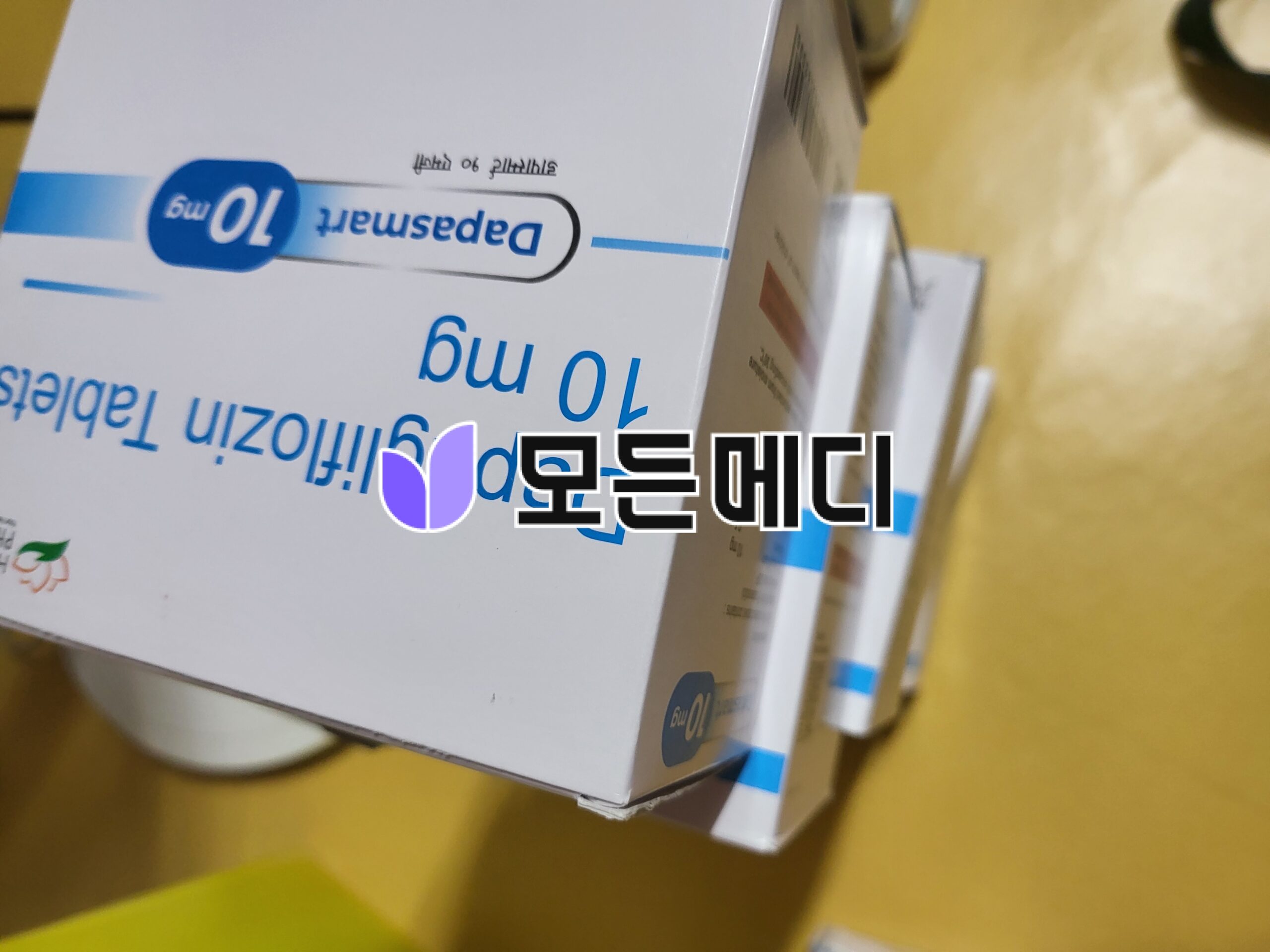Close-up of a white medication box on a yellow surface, showing blue branding and a prominent '10 mg' label.